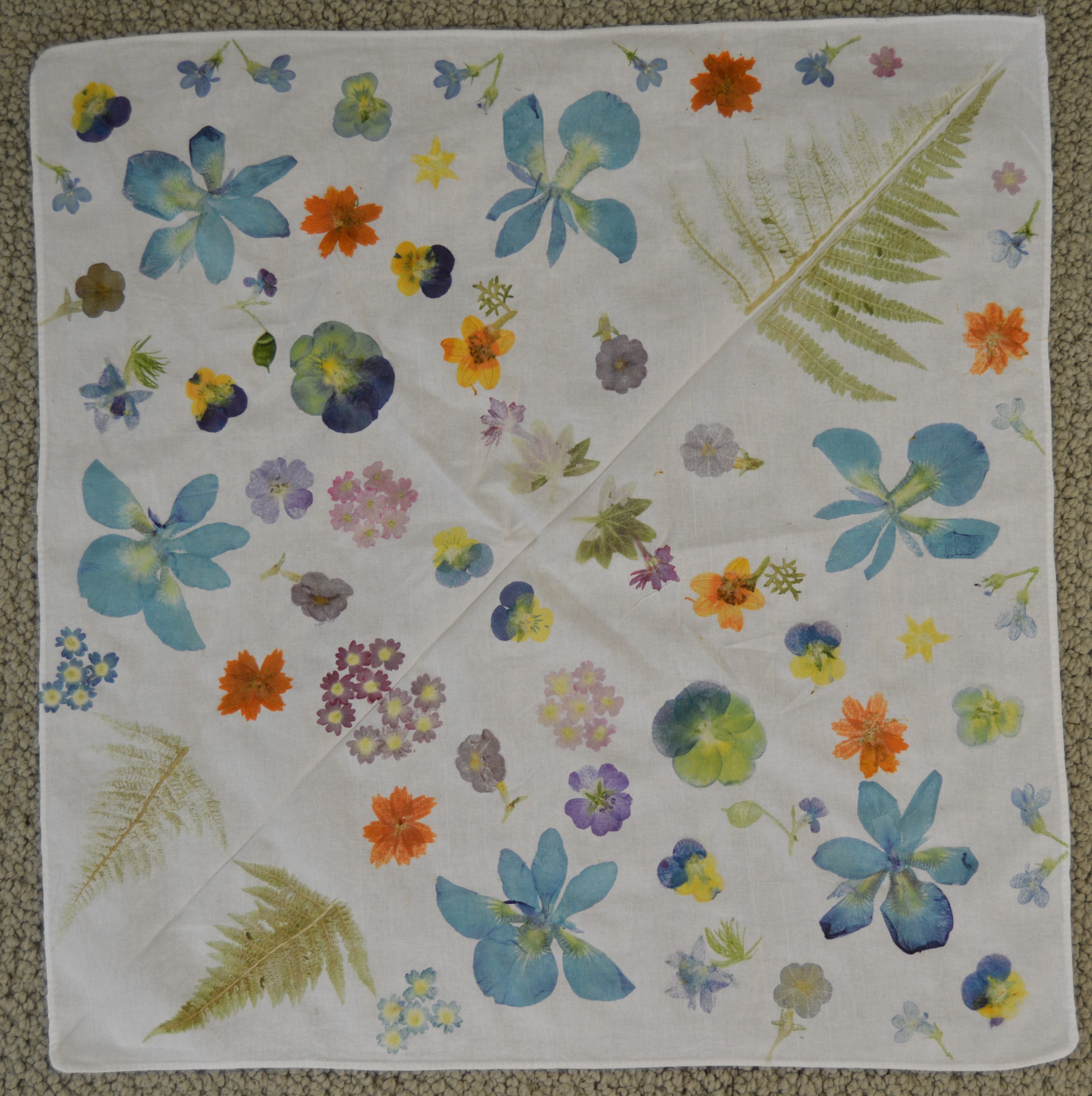 Spring Flowers Bandana — a light-colored bandana with a mirrored botanical pounding pattern of blue blossoms, orange flowers, pansies, and fern leaves