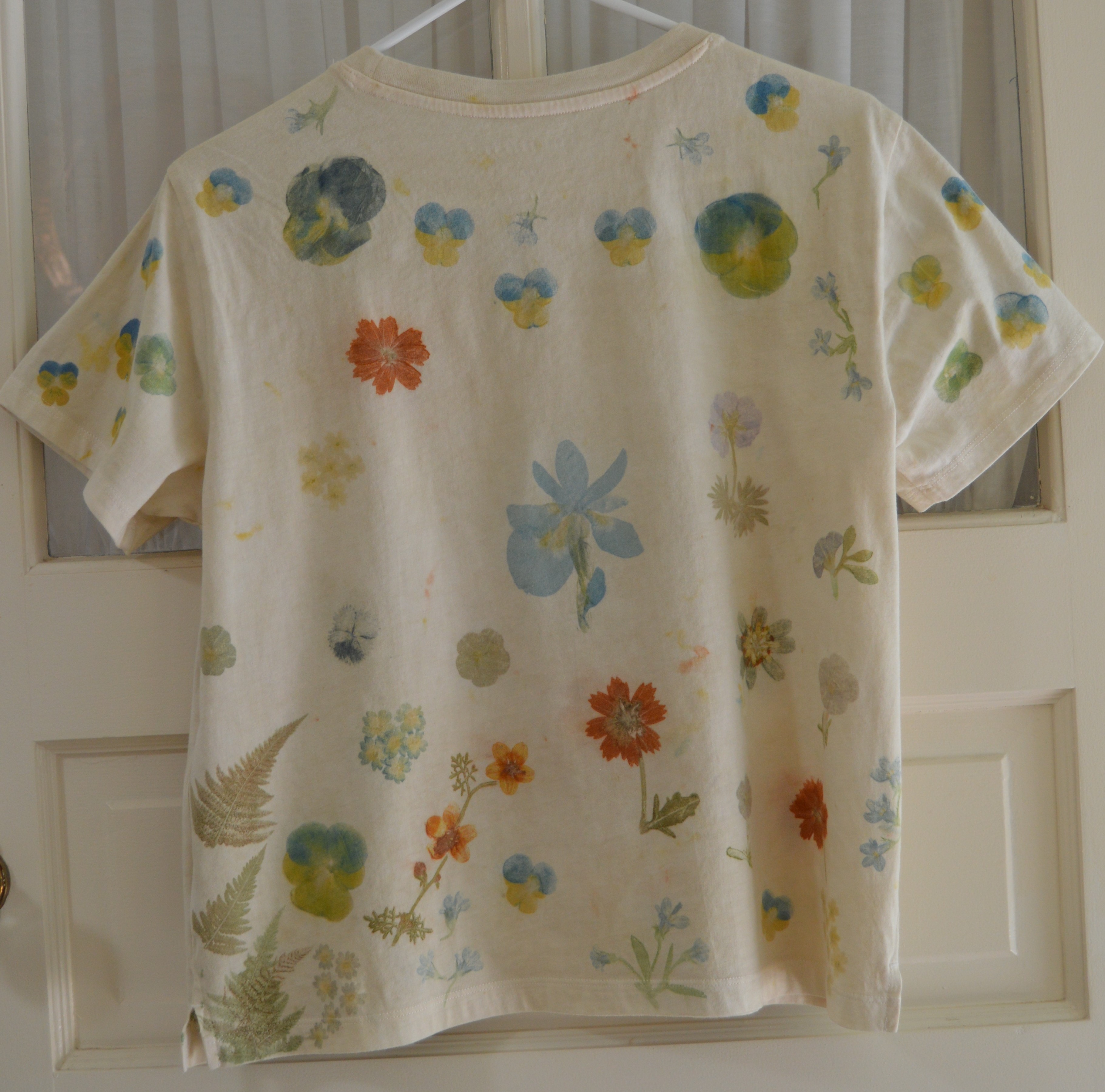 Back of a cream combed-cotton T-shirt pounded with colorful spring flora motifs — mirror image of the front